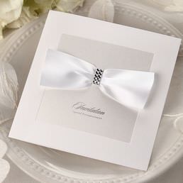 Lightly textured card printed in calligraphic raised ink lettering, attached to a gorgeous card with silk screened front cover, adorned with a white bow and gems
